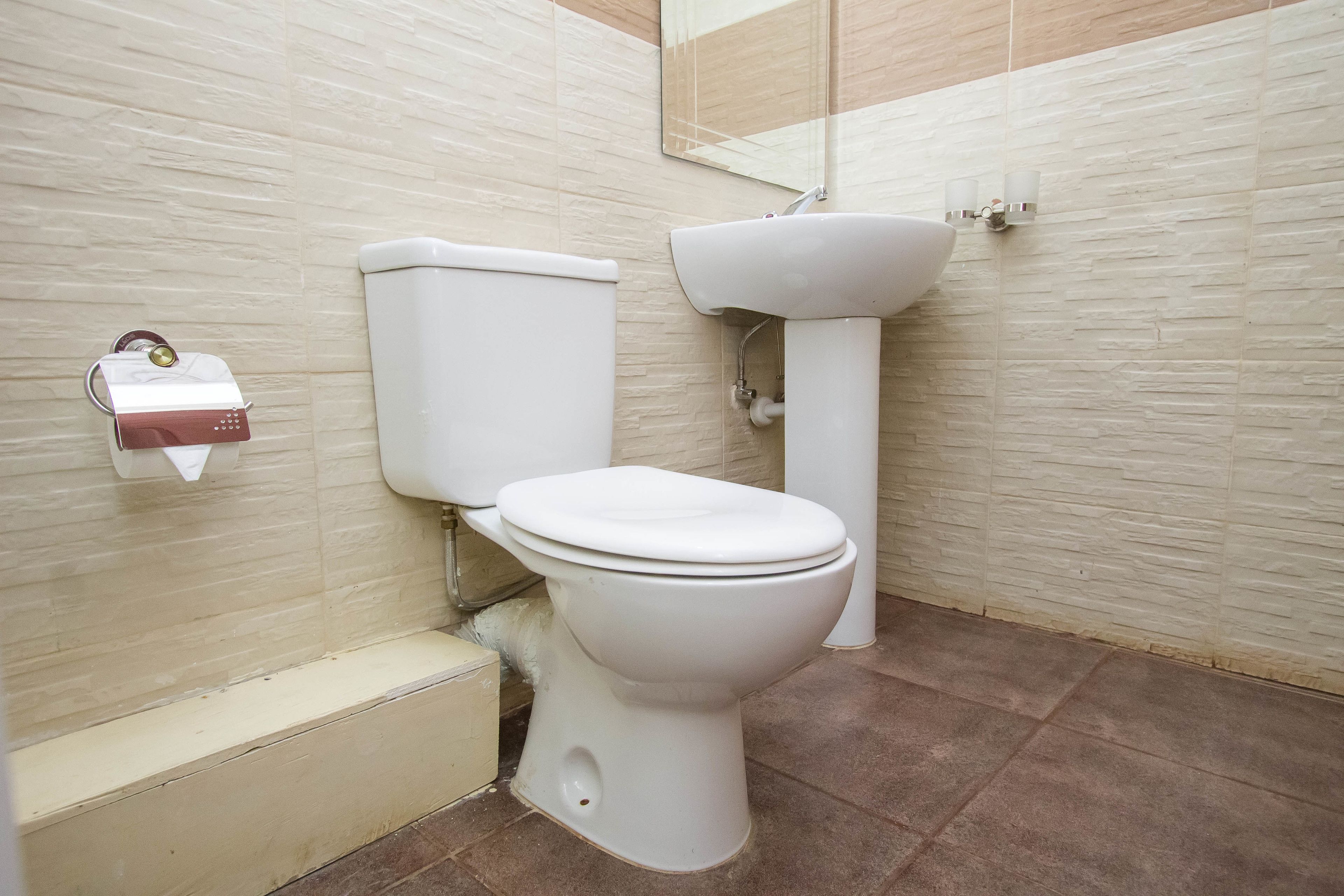 A bathroom with a toilet, sink, and a mirror on the wall.