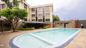 A swimming pool with a stone deck, surrounded by a building with multiple windows and air conditioning units. - Pinecone Hotel (Kisumu)