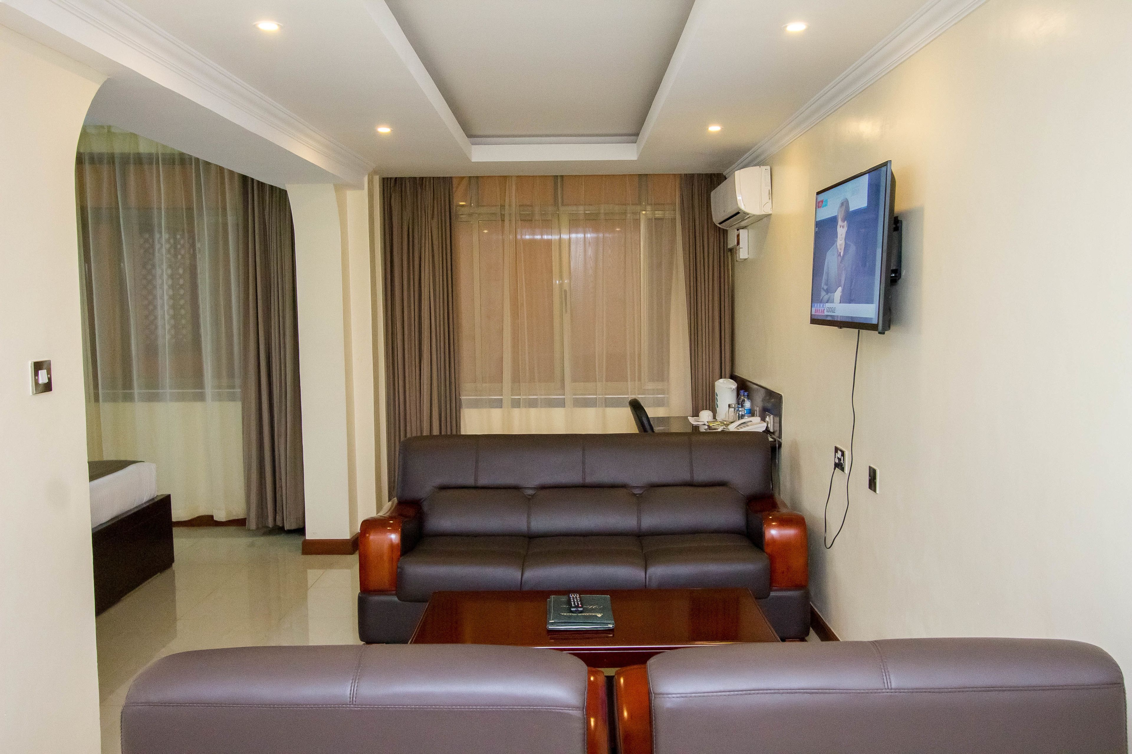 Quarto de hotel moderno com sofá, mesa de centro, televisão fixada na parede e janela com cortinas.