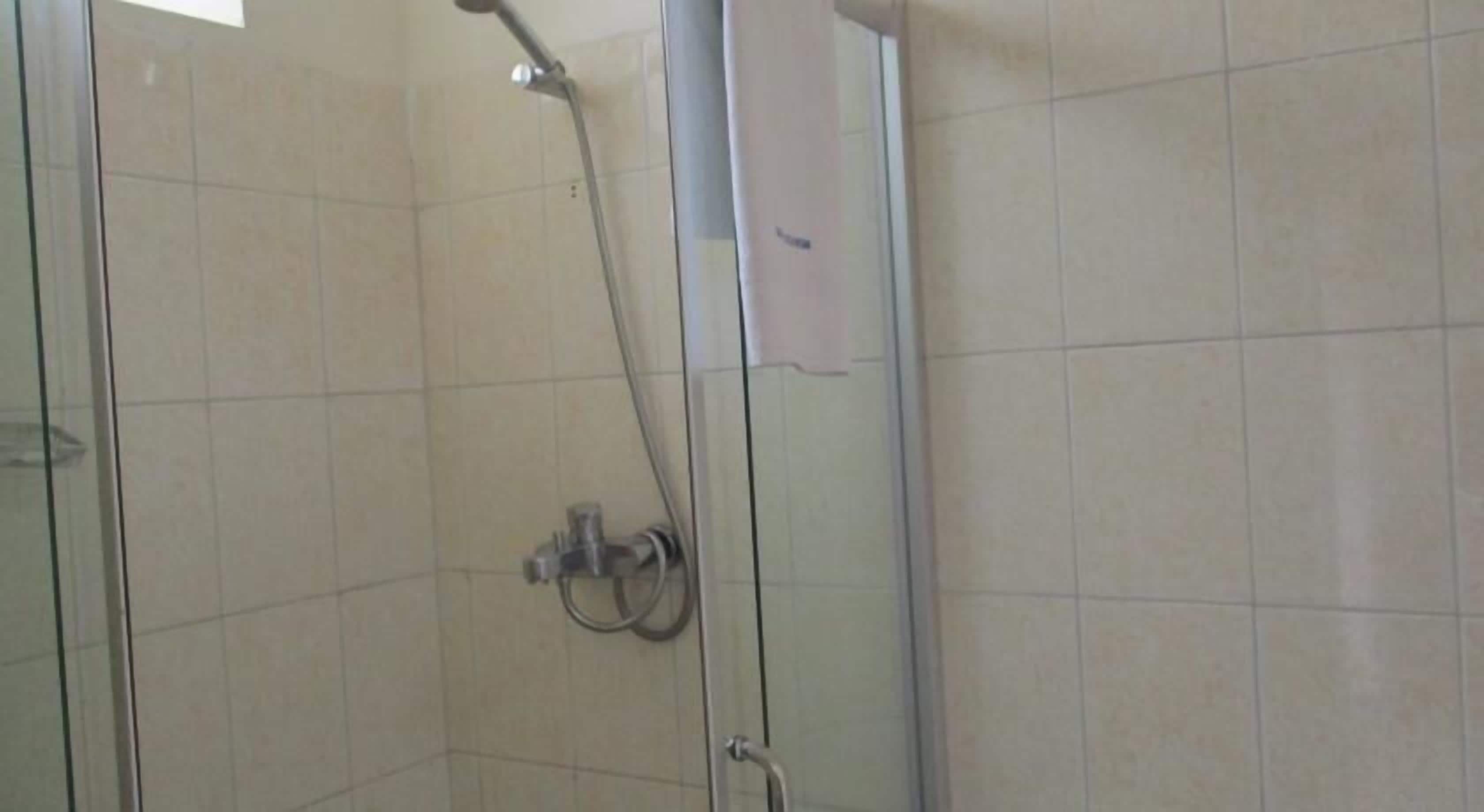 Une douche fermée par des parois en verre, dotée d’un pommeau de douche à main et d’un robinet mural.