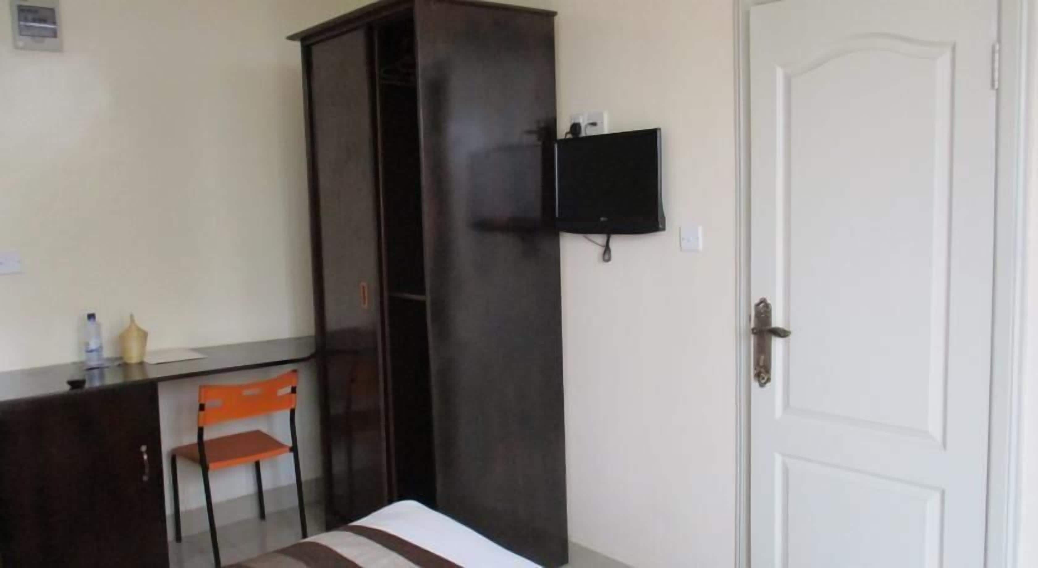 Una habitación con cama, escritorio y silla, armario, televisor montado en la pared y una puerta.
