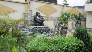 Ein Garten mit einer großen Gorilla-Statue, umgeben von verschiedenen Pflanzen und einer dekorativen Wand mit geometrischen Mustern.