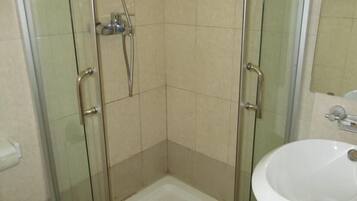 A corner shower with glass doors, a white sink, and a mirror above the sink.