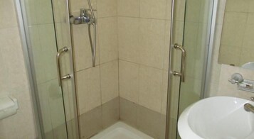 Una ducha en esquina con puertas de vidrio, un lavamanos blanco y un espejo sobre el lavamanos.