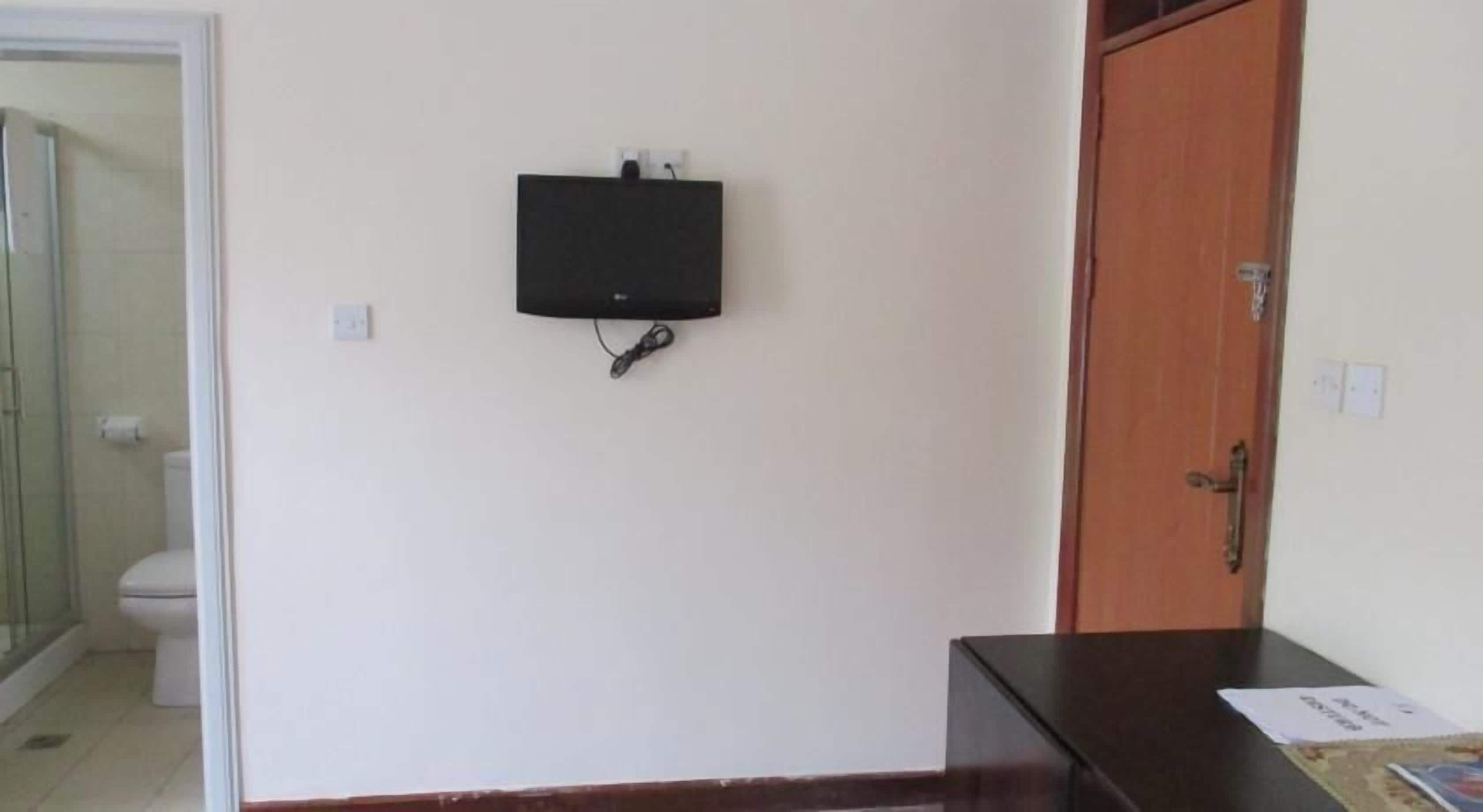 A room with a wooden door, a black electronic device mounted on the wall, and a small table with a booklet on it.