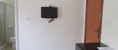 A room with a wooden door, a black electronic device mounted on the wall, and a small table with a booklet on it.