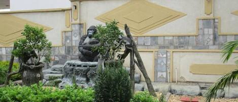 A statue of a gorilla holding a child, surrounded by greenery and a decorative wall with geometric patterns.