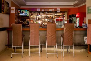 A bar area with a television screen, a variety of liquor bottles, and a refrigerator.