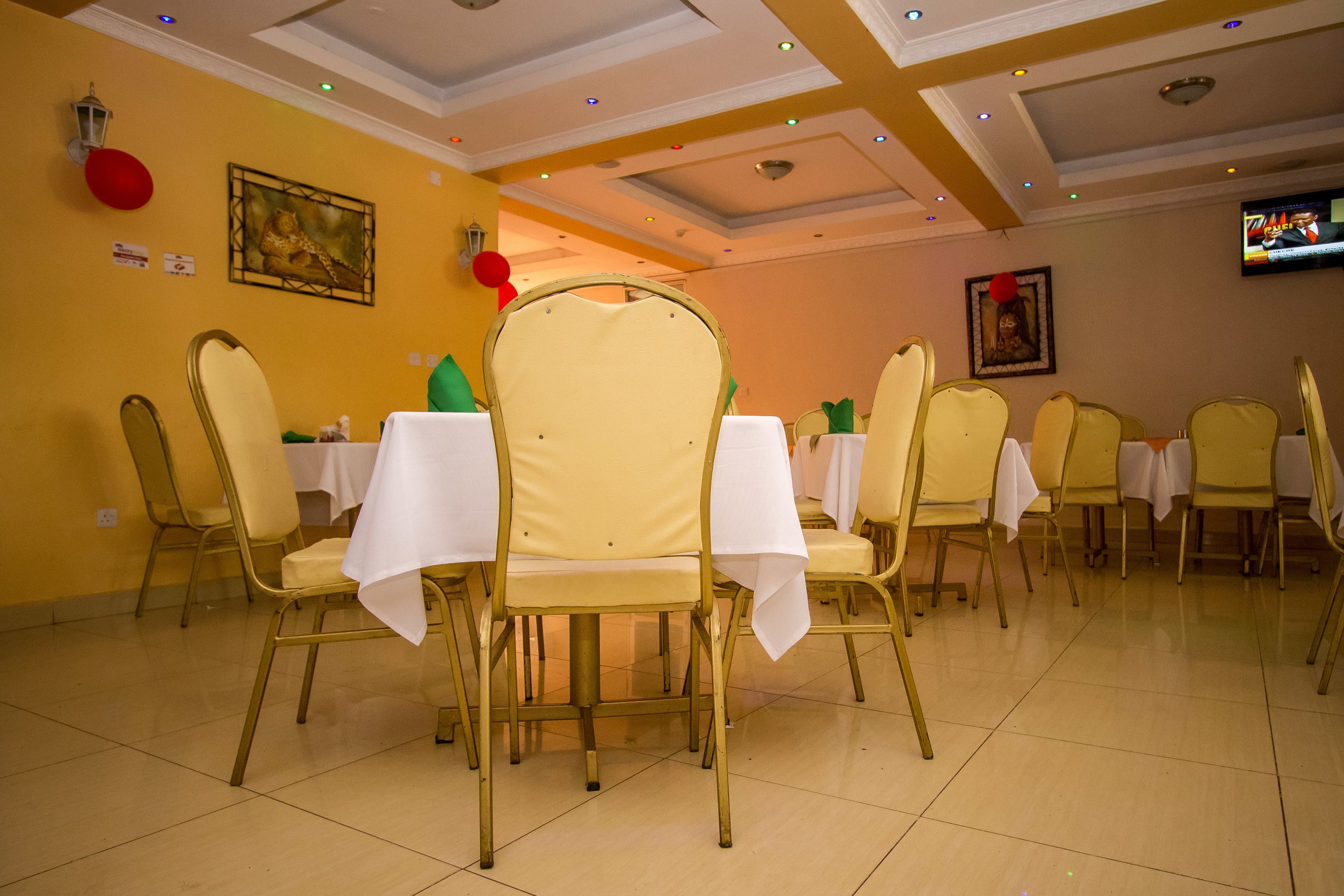 Zona pranzo con tavoli apparecchiati per sei persone, ognuno con tovaglia bianca e sedie dorate.