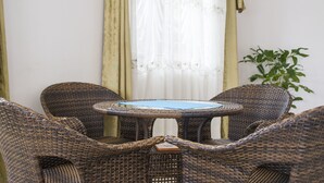 A wicker dining set with a table and four chairs, positioned in front of a window with sheer curtains. - Spannet Suites (Mbarara)