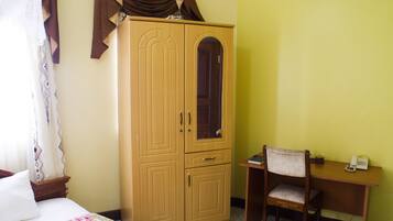 A bedroom with a bed, a wooden wardrobe, a desk with a chair, and a telephone.