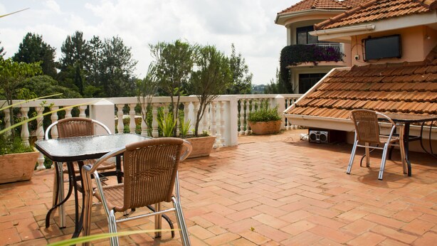 An outdoor patio with a table and chairs, potted plants, and a tiled roof. - Spannet Suites (Mbarara)
