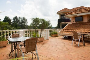 An outdoor patio with a table and chairs, potted plants, and a tiled roof. - Spannet Suites (Mbarara)