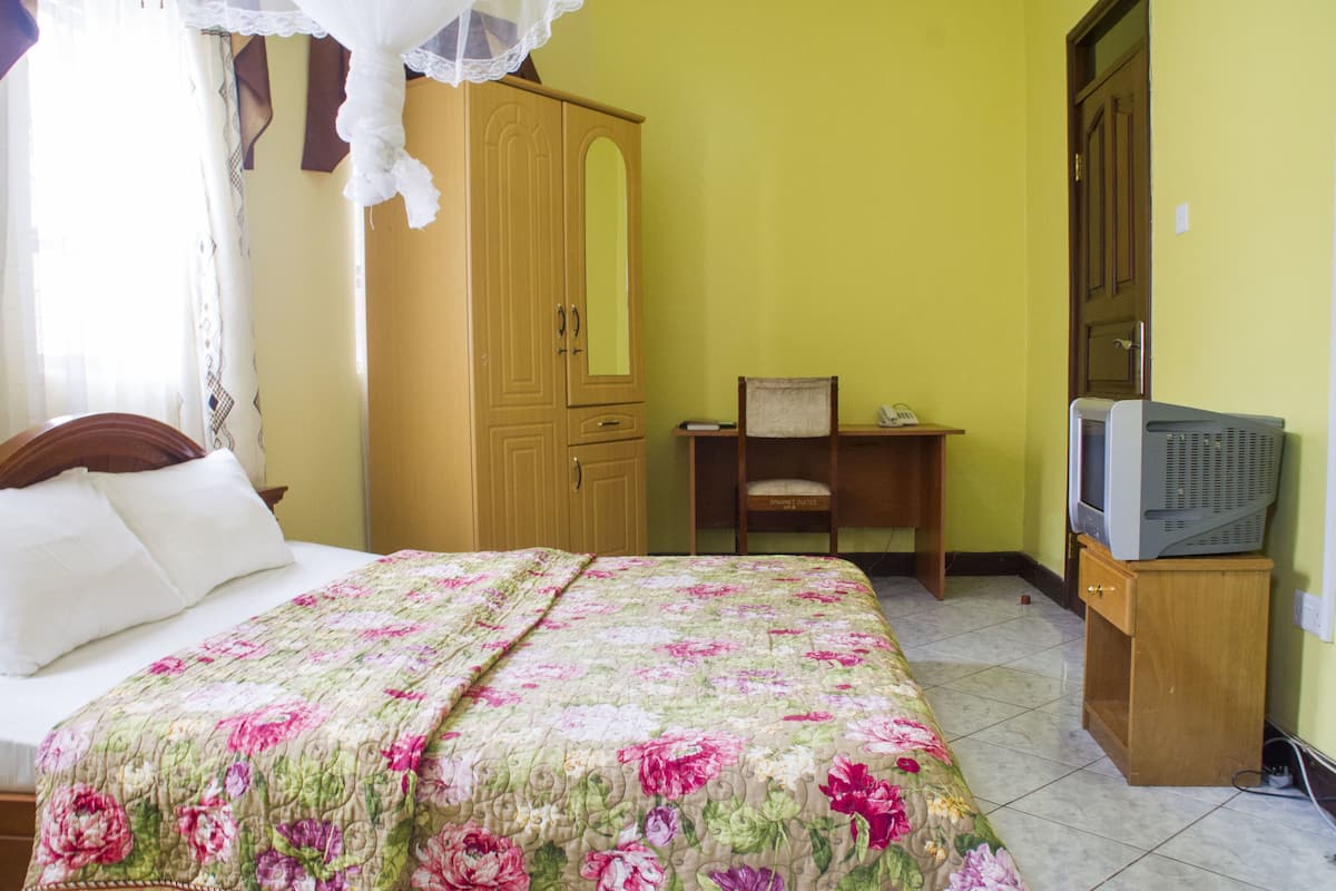 A bedroom with a bed, a wooden wardrobe, a chair, and a television.