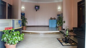 A reception area with a reception desk, a television mounted on the wall, and potted plants. - Spannet Suites (Mbarara)