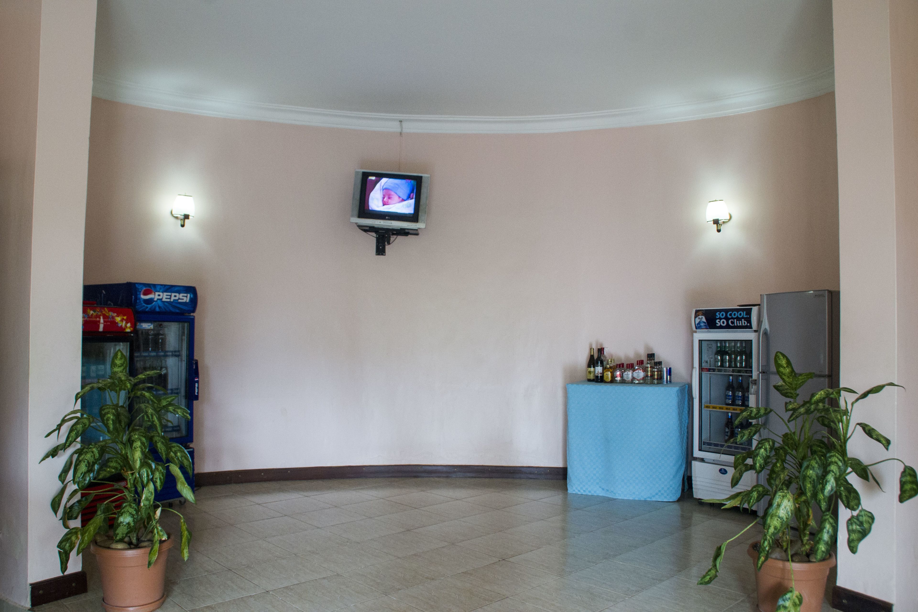 A lobby with a television mounted on the wall, vending machines, and potted plants.
