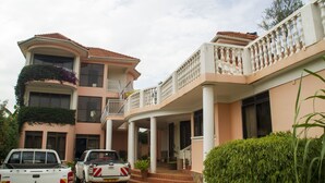 A multi-story house with a balcony, a driveway, and parked vehicles. - Spannet Suites (Mbarara)
