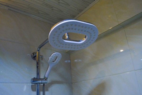 Chuveiro com um chuveiro manual e um chuveiro fixo no teto, em um banheiro revestido com azulejos.