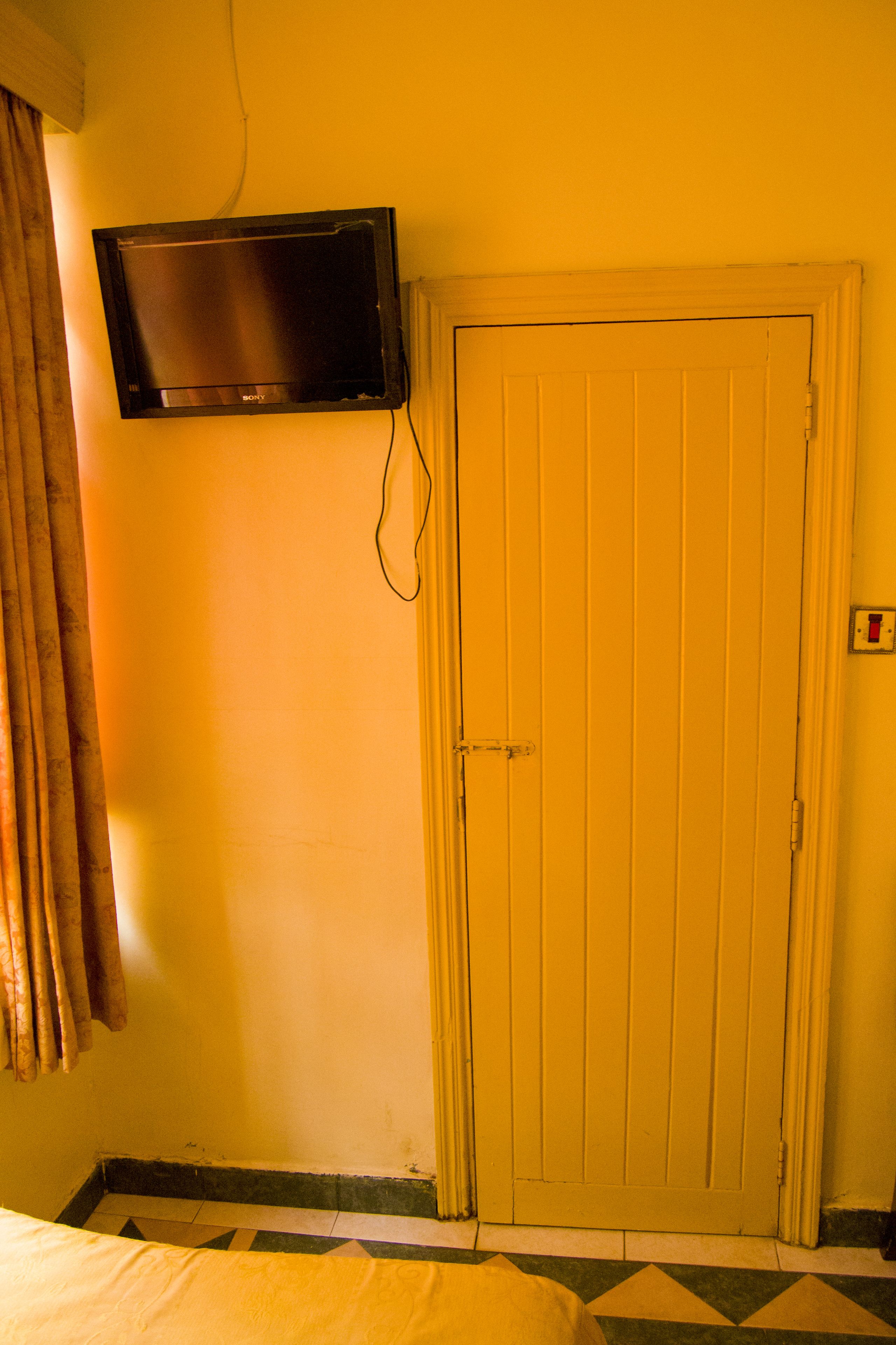 A room with a bed, a television mounted on the wall, and a closed door.