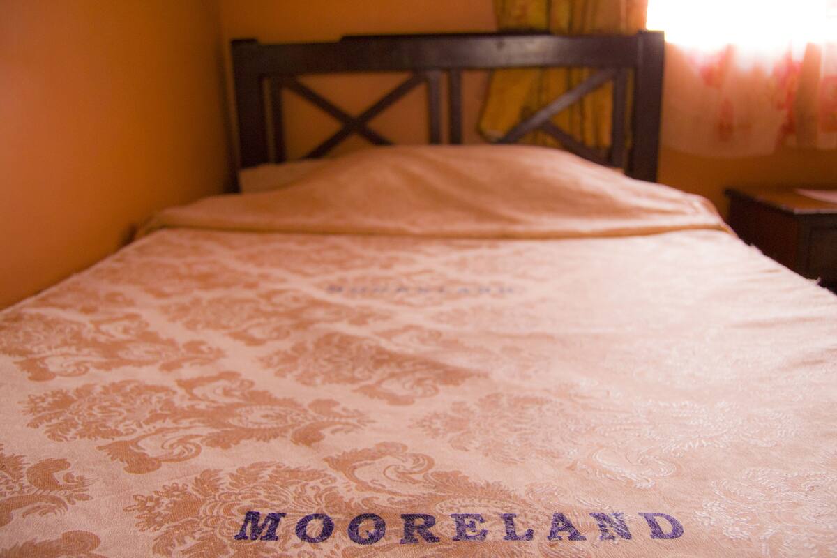 Un lit recouvert d’une couvre-lit à motifs, sur lequel est brodé le mot « MOORELAND ».