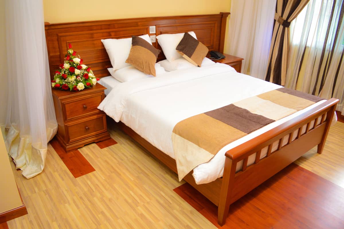 A neatly made bed with a wooden headboard, a bedside table with a telephone, and a floral arrangement on the nightstand.