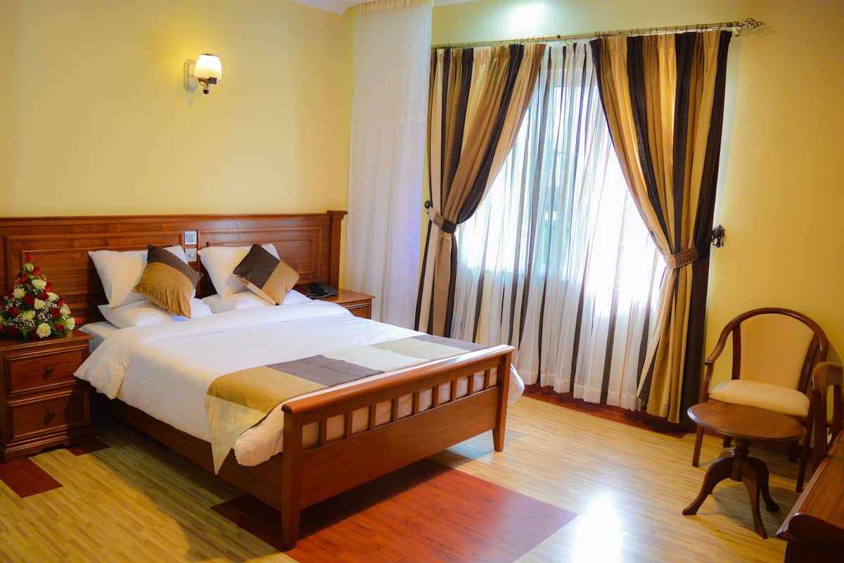 A neatly made bed with a wooden headboard, a nightstand with a vase of flowers, and a chair.