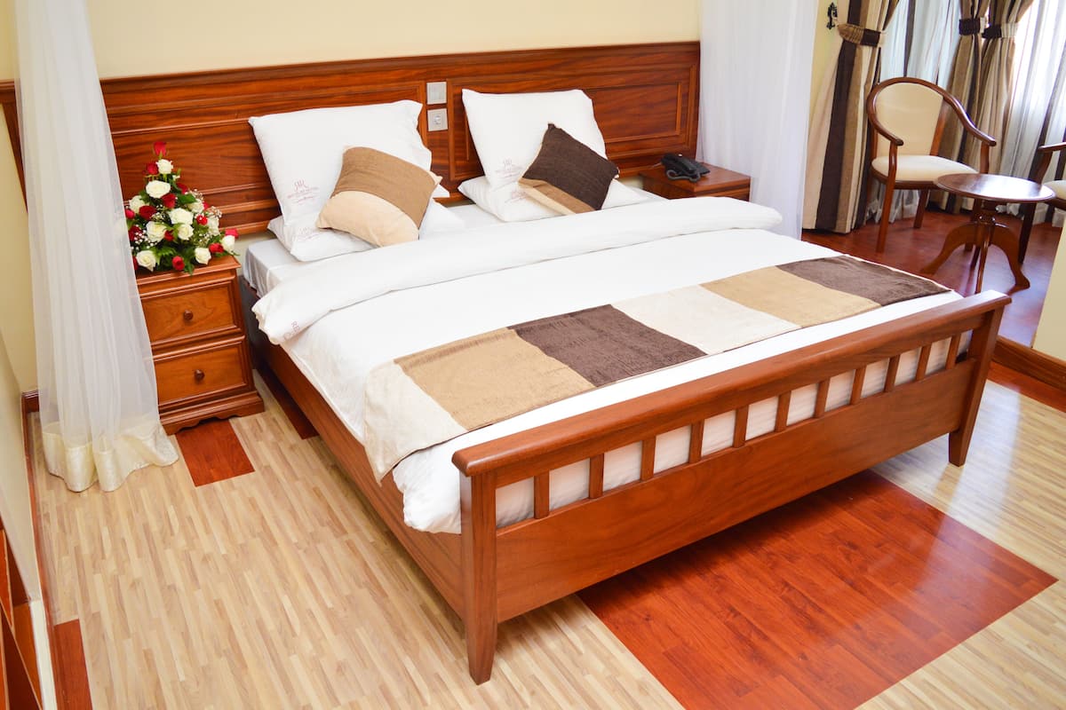 A neatly made bed with a wooden headboard, a bedside table with a lamp, and a chair in a hotel room.