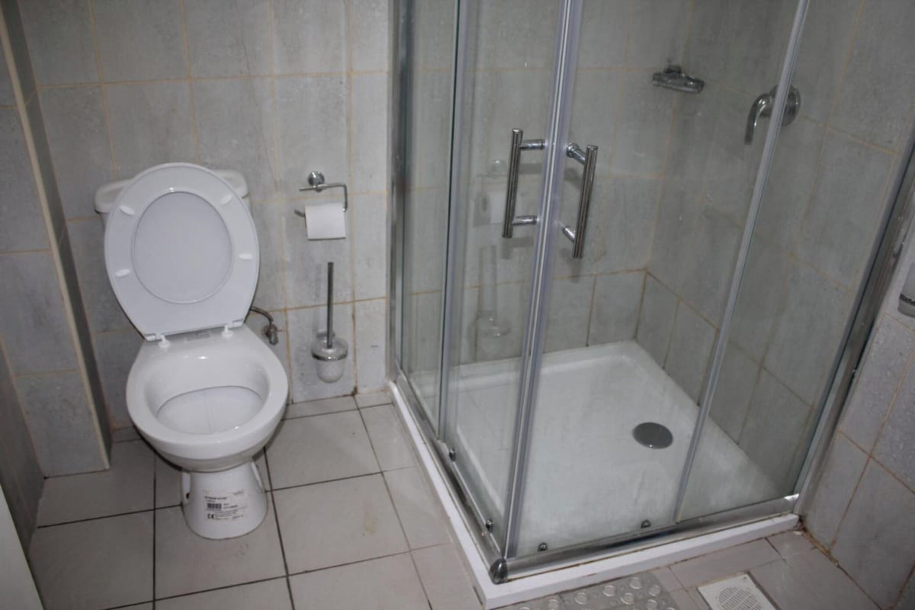 Un baño con inodoro, ducha con mampara de vidrio y piso de baldosas.