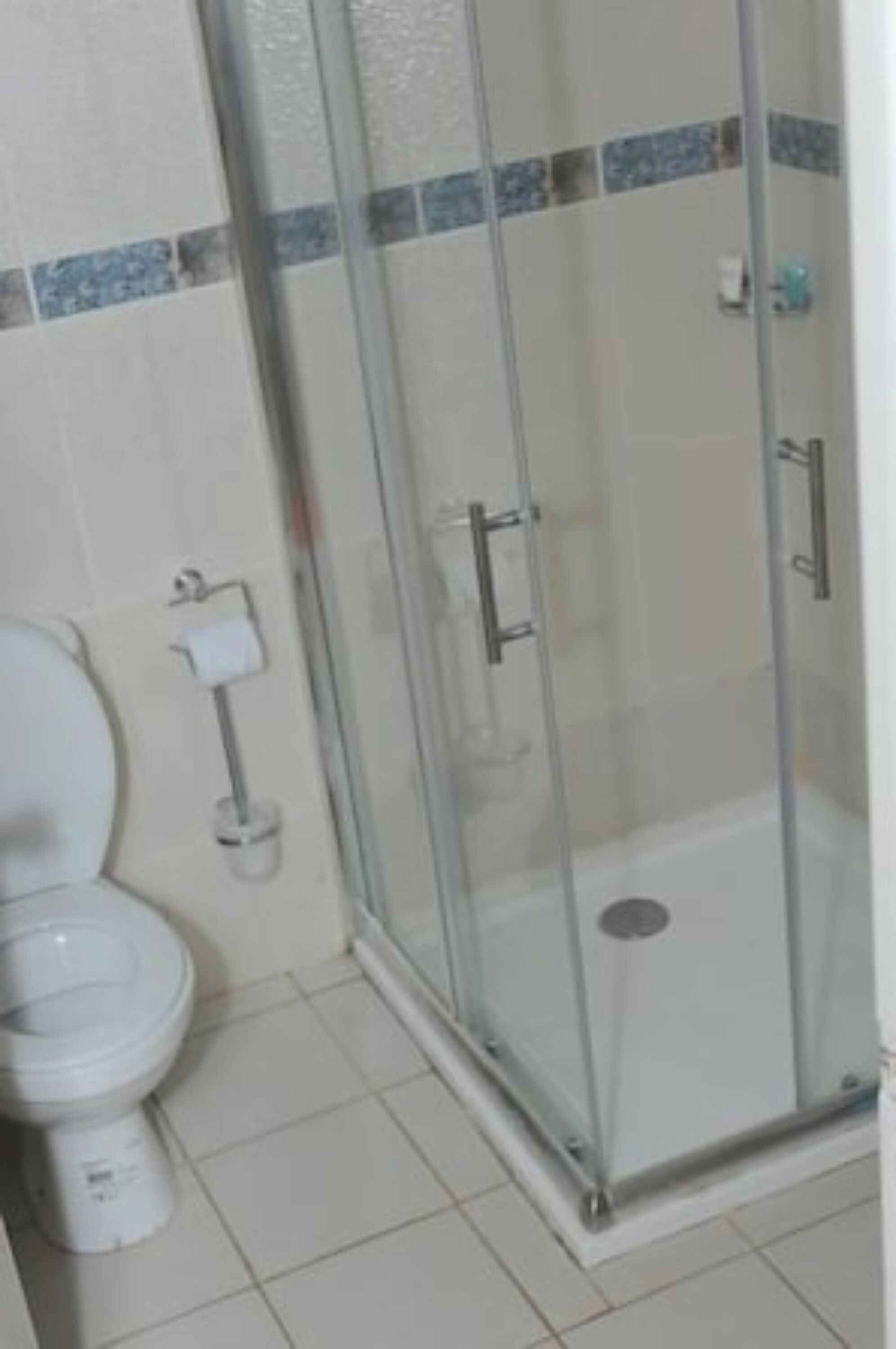 Un baño con inodoro, ducha envuelta en vidrio y suelo de baldosas.