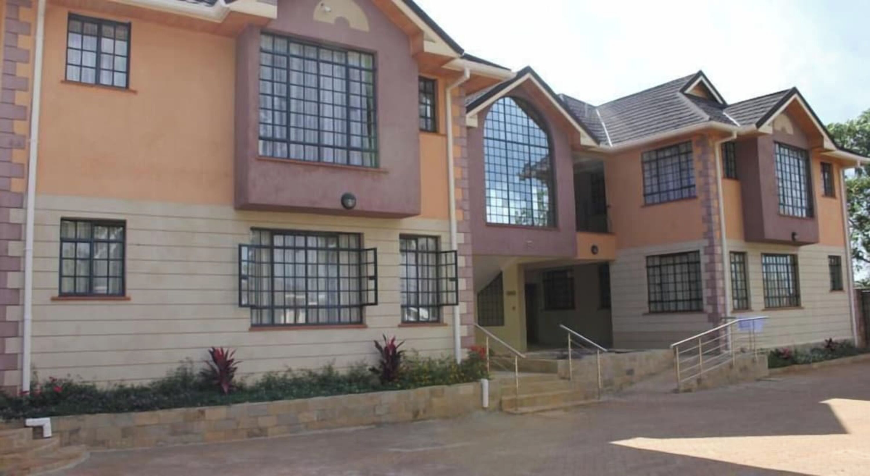 A multi-story building with a flat roof, large windows, and a staircase leading to the entrance.