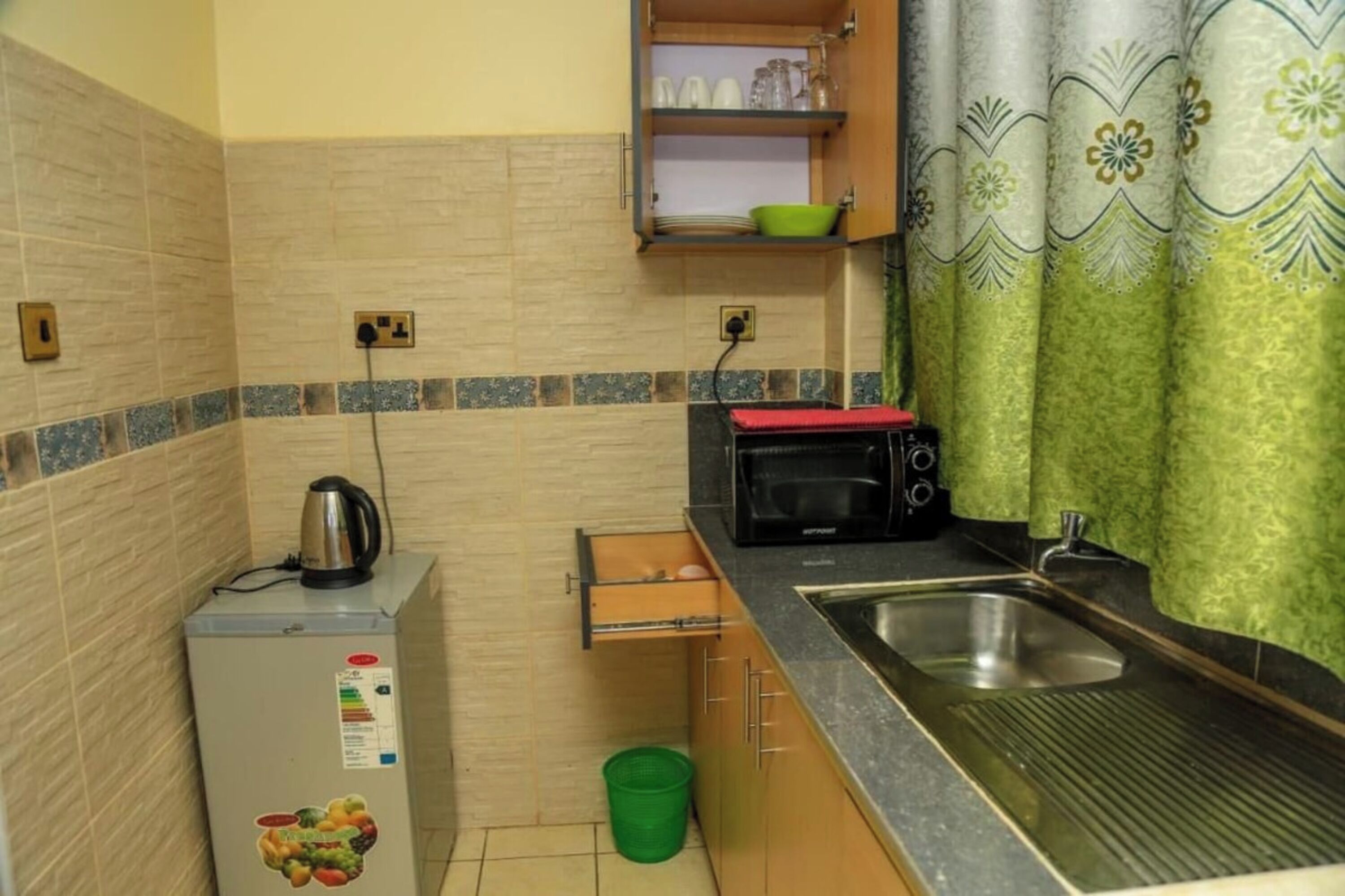 A compact kitchen with a refrigerator, microwave, sink, and a small cabinet above the counter.