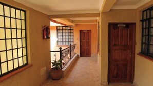 A hallway with a tiled floor, a wooden door labeled "ROOM 1", and a window with a grid pattern. - Davis Court Nyeri (Nyeri)