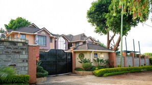 A two-story house with a gated driveway, a well-maintained lawn, and a large tree. - Davis Court Nyeri (Nyeri)