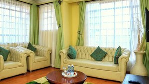 A living room with two beige sofas, a coffee table, and a green rug. - Davis Court Nyeri (Nyeri)