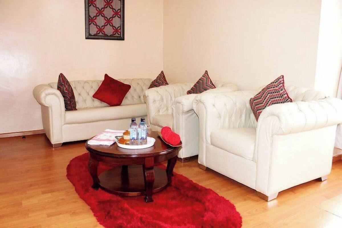 A living room with two white sofas, a red rug, and a coffee table with bottles and a plate.