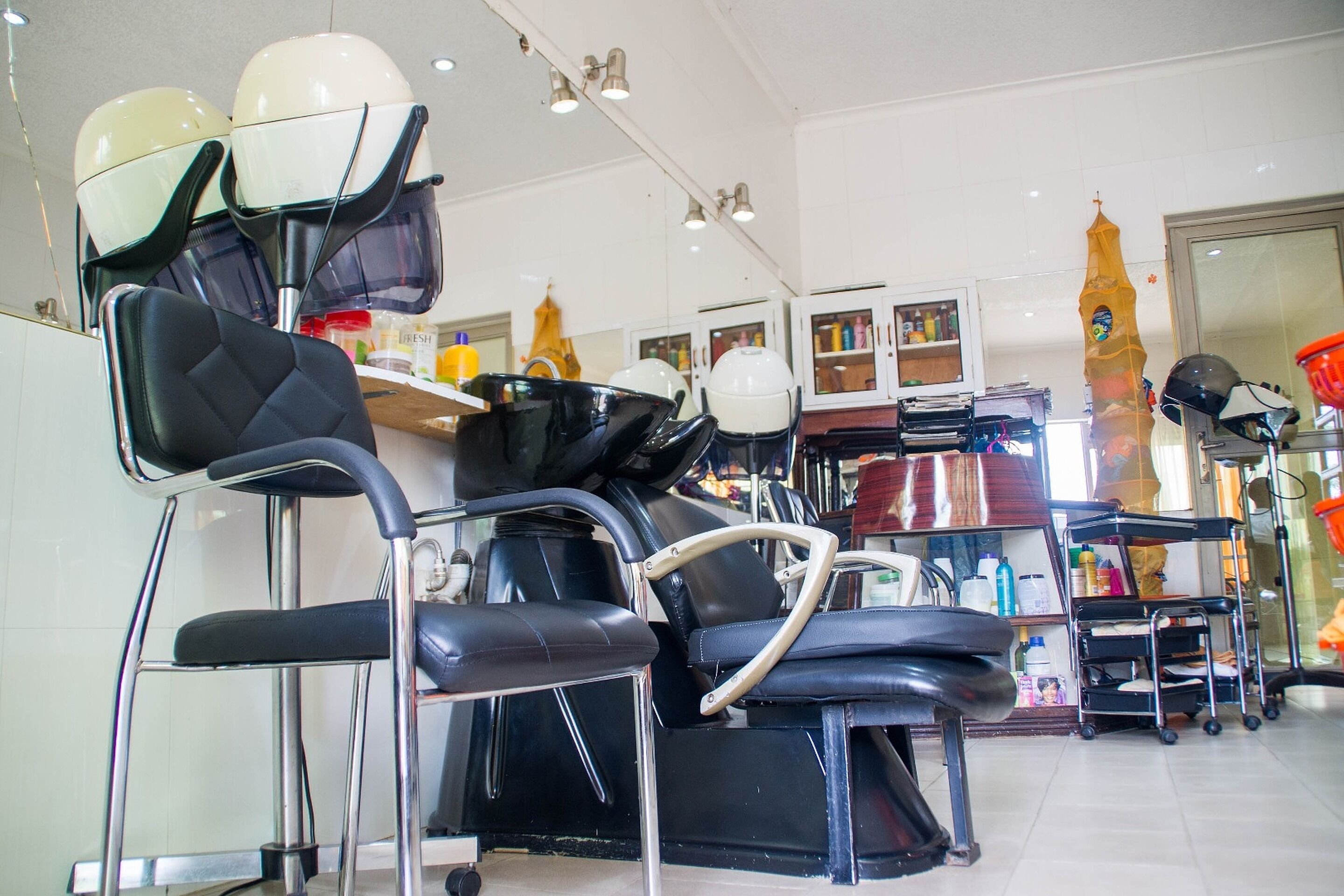Un salón con varias sillas de peluquería negras, una barra con diversos productos para el cabello y un espejo.