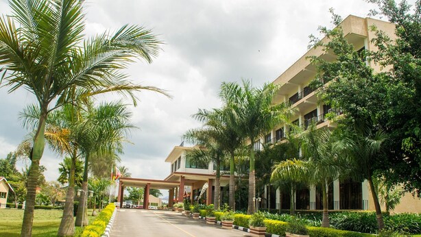 A hotel entrance with a covered walkway, palm trees, and a well-maintained lawn. - Lake View Resort Hotel (Mbarara)