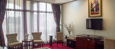 A hotel room with a large bed, two armchairs, a small round table, a desk, a television, and a painting on the wall.