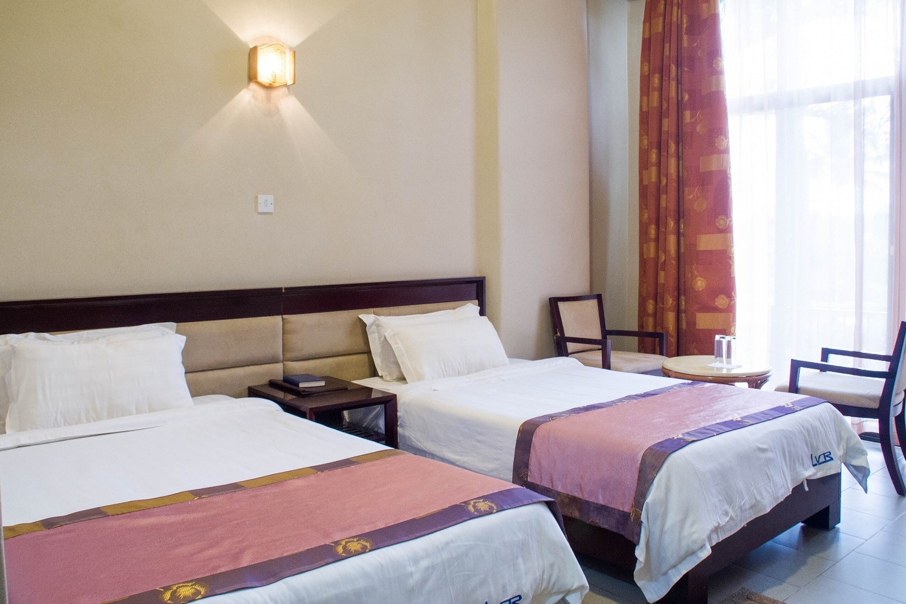 Ein Hotelzimmer mit zwei Betten, einem Nachttisch, einem Sessel und einem kleinen Tisch.