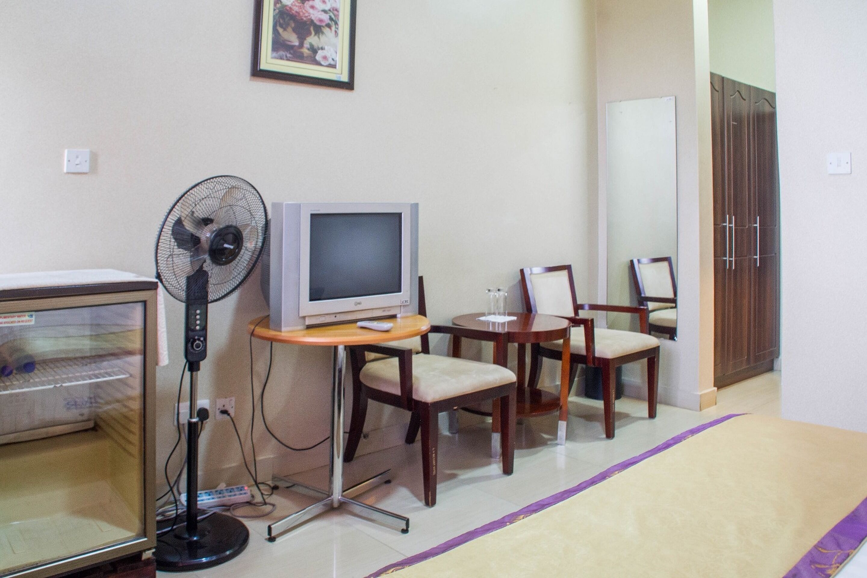 A room with a television, a fan, a small table, two chairs, and a door.