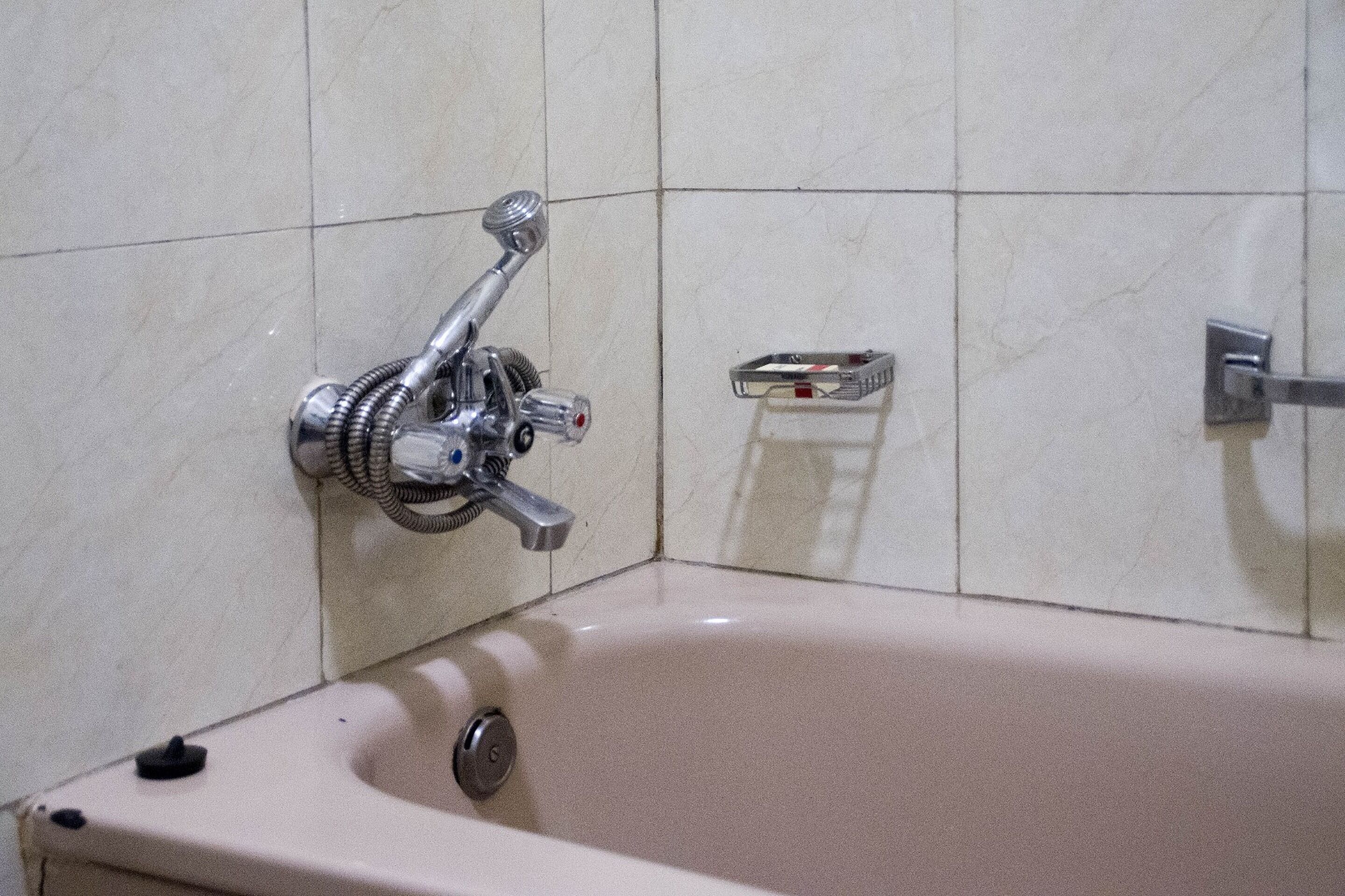 Un baño con bañera, ducha de mano y jabonera en la pared.