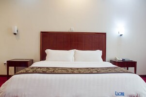 Habitación de hotel con una cama grande, un cabecero de madera, dos mesitas de noche y un teléfono sobre una de ellas.