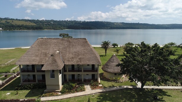 A building with a thatched roof, surrounded by a well-maintained lawn and a view of a large body of water. - Victoria Forest Resort (Bugala Island)