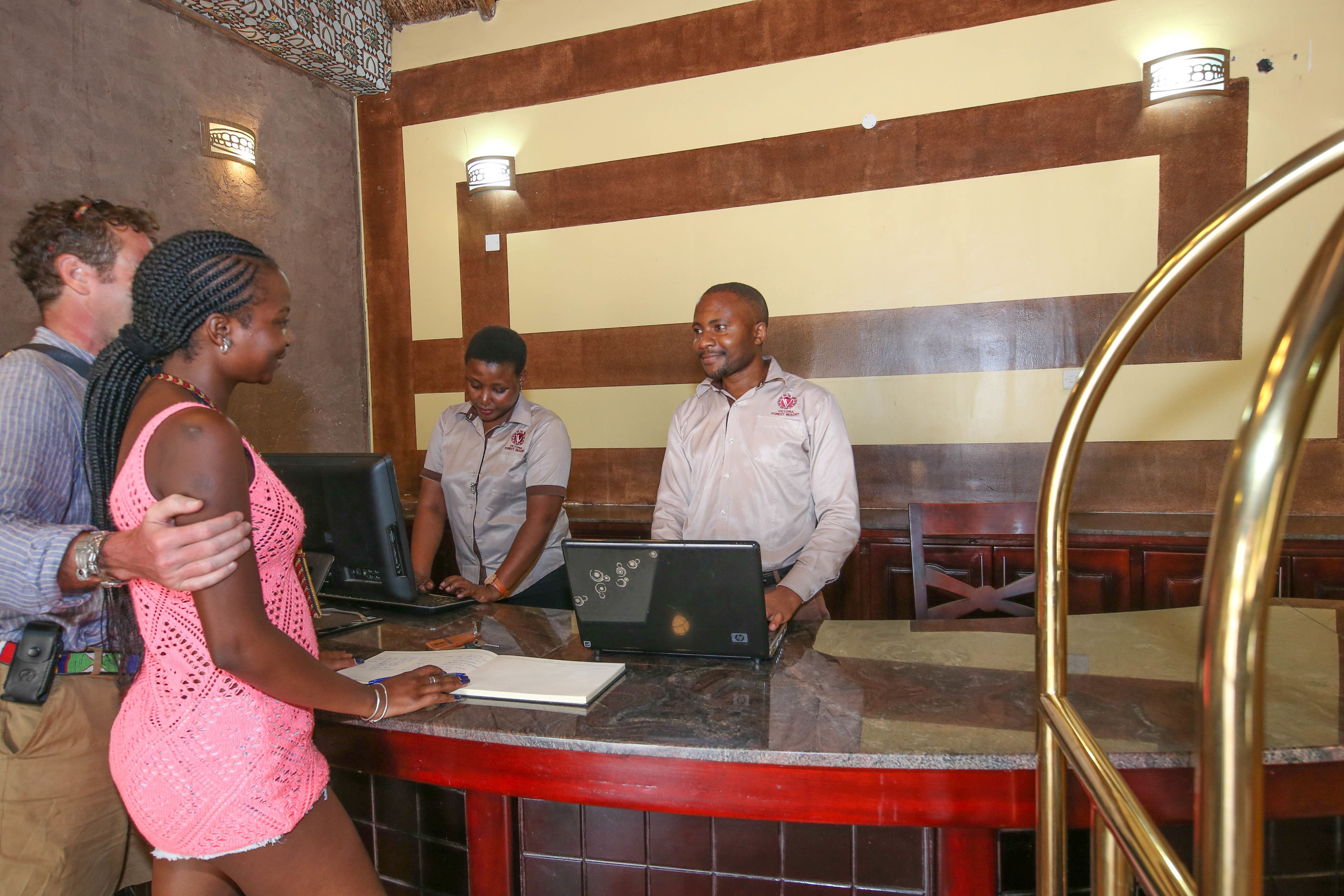 A reception area with a counter, two staff members, and a guest.