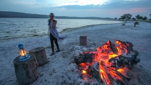 A person standing near a campfire on a sandy beach with a body of water in the background. - Victoria Forest Resort (Bugala Island)