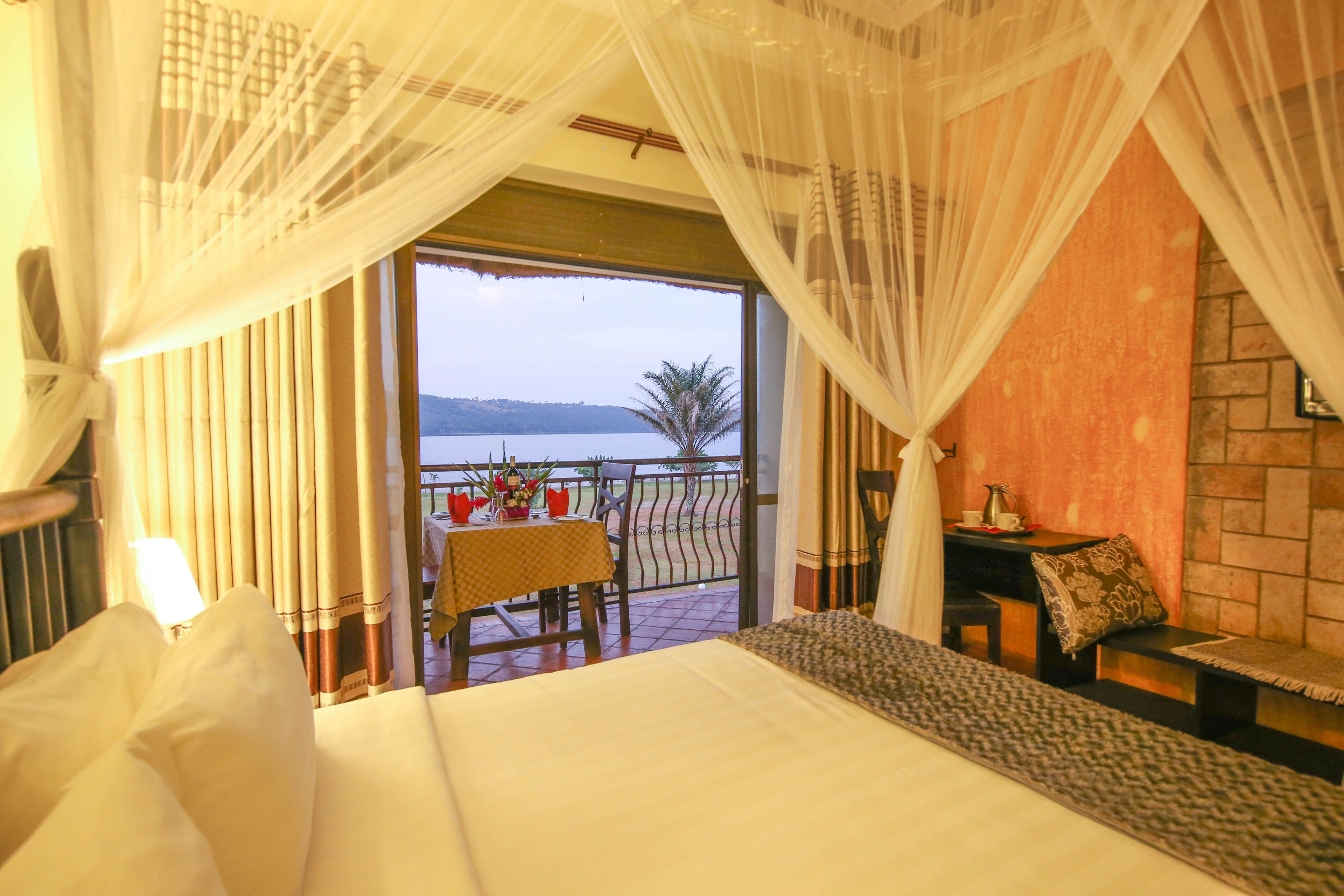 A hotel room with a bed, a small table with a chair, a sofa, and a balcony with a view of the sea.