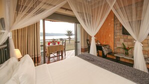 A bedroom with a large bed, a balcony with a table and chairs, and a view of the sea. - Victoria Forest Resort (Bugala Island)