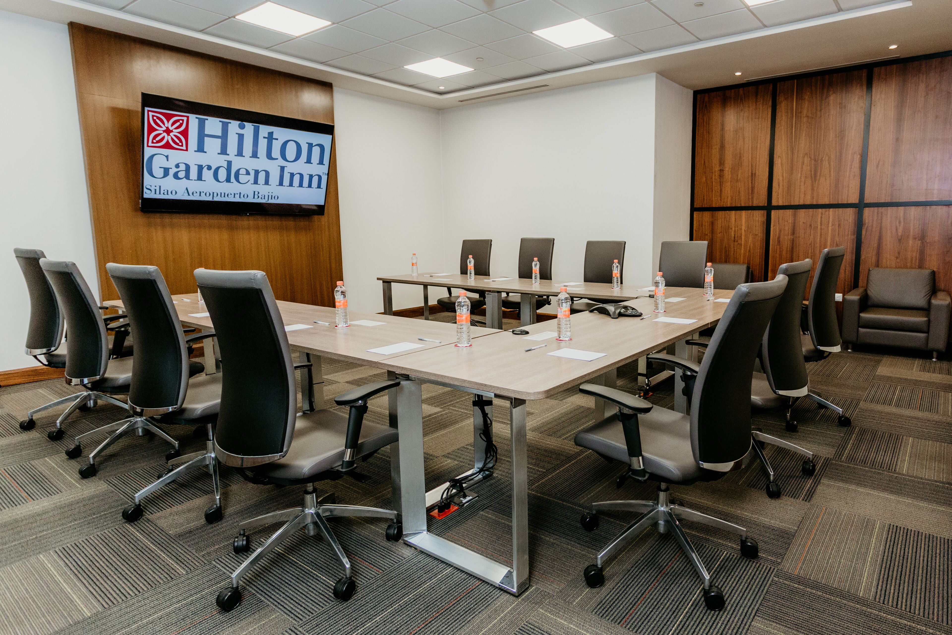 A conference room with a long table, multiple chairs, and a Hilton Garden Inn sign on the wall.