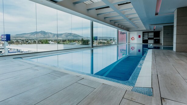 A modern indoor swimming pool with a view of mountains, a reception area, and a large glass wall. - Hilton Garden Inn Silao Aeropuerto Bajio (Silao)