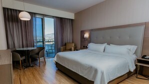 A hotel room with a large bed, a desk with two chairs, a lamp, and a view of the city through the window. - Hilton Garden Inn Silao Aeropuerto Bajio (Silao)